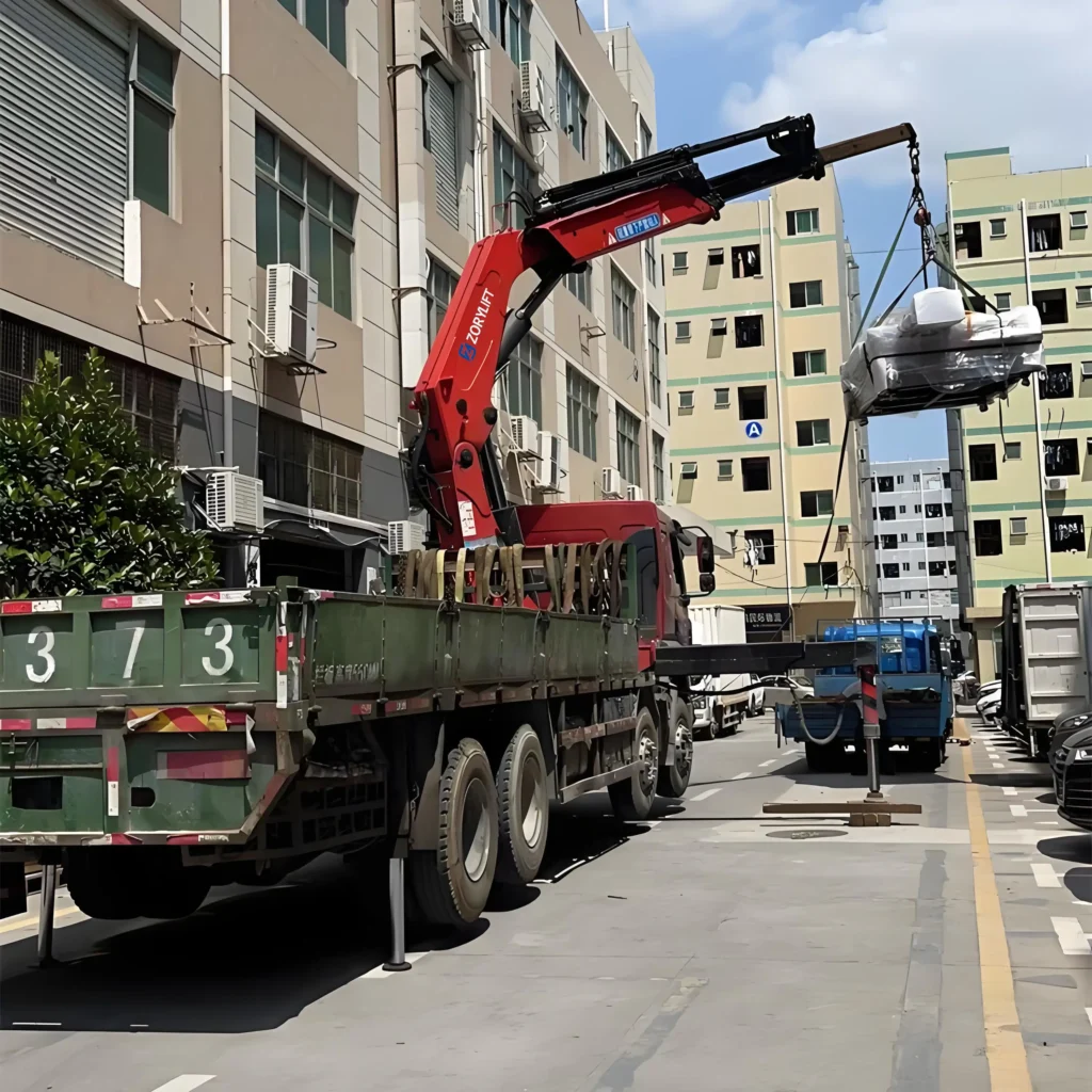 Customer using a red truck mounted knuckle boom crane (knuckle crane truck) for material handling (moving loads) in a city environment with buildings. This showcases the functionality of a truck loader crane in logistics or construction applications.