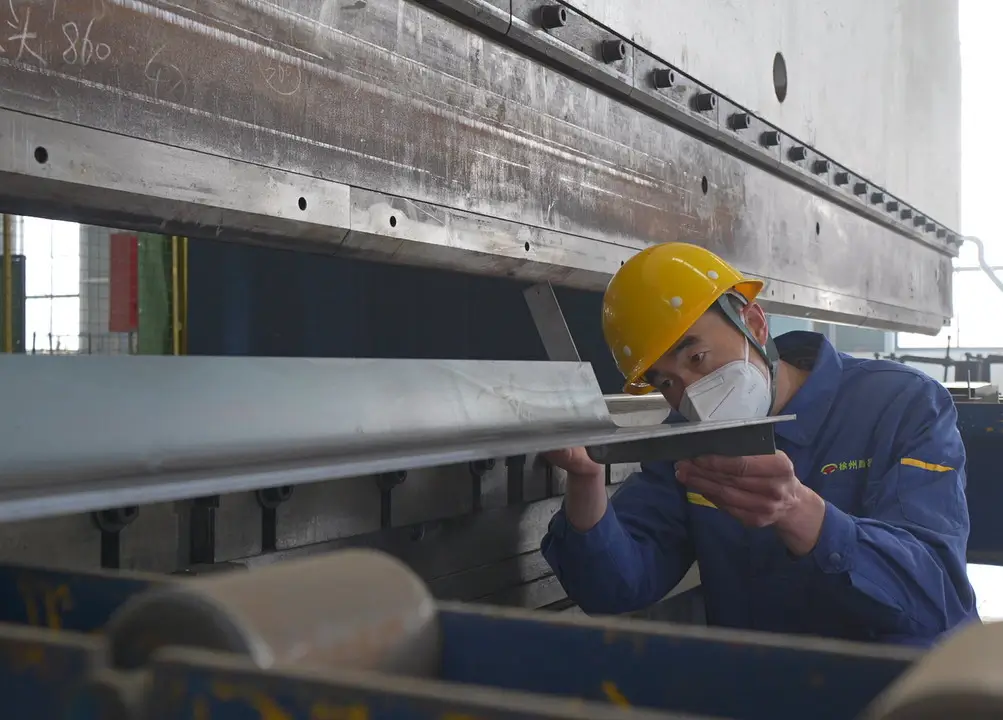 Precision truck mounted cranes manufacturing process: A technician in workwear checks the angle of a recently bent metal component, ensuring it meets the accuracy requirements set by technical support to guarantee product quality.