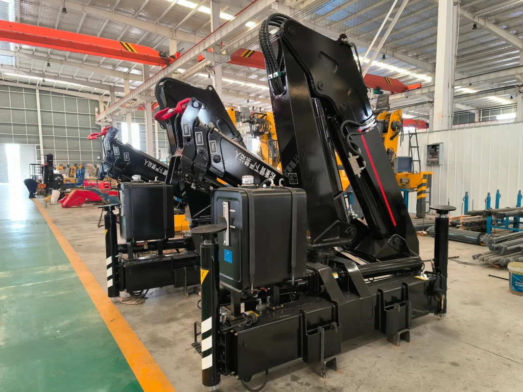 Factory floor view of several black SQZ132A.3 knuckle boom units, a type of crane machine, awaiting final assembly for a customer's order.