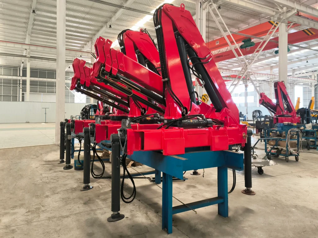 Factory production line featuring multiple red SQZ68B.3 3.2-ton loader cranes with articulating knuckle booms , mounted on blue stands before final assembly as vehicle mounted cranes.